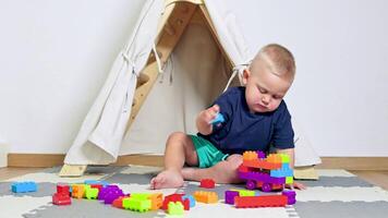 A joyful toddler is fully focused on constructing colorful block towers while happily sitting on a soft, playful mat inside a charming little tent. Imagination is truly at play video