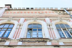 Bottom view to architectural detail of historic building with ornate windows and weathered facade photo