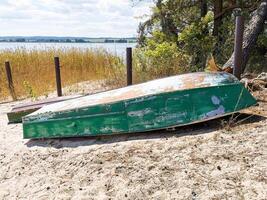 Abandoned green wooden boat resting on sandy shore surrounded by tall grass and water photo