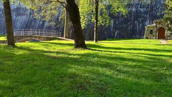 A tranquil park scene showcasing a charming stone structure, lush vibrant grass, and trees near a dam wall photo
