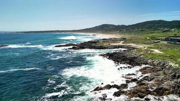 Capture the breathtaking beauty of the coast with waves dramatically crashing upon the rocky shores beneath clear skies photo