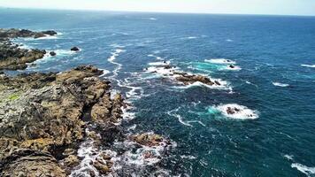 Experience stunning aerial footage of a rocky coastline merging with turquoise sea waves for a picturesque view photo