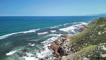 The stunning seaside view shows powerful waves crashing against rugged cliffs under a clear blue sky photo