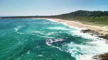 This aerial view showcases a stunning beach with crashing waves, golden sand, and lush green hills behind photo