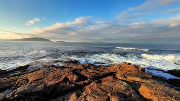 A breathtaking view showcasing the waves fiercely crashing on rugged rocks during a vibrant sunrise by the sea photo