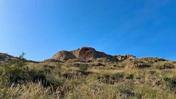 The breathtaking view of rocky hills adorned with golden grass stretches out beautifully beneath a clear blue sky photo