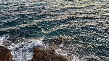 A serene ocean view featuring gentle waves and a stunningly beautiful sunset over a rocky coastline photo