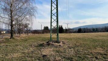 A tall electricity transmission tower rises prominently in an expansive open field that is surrounded by nature photo