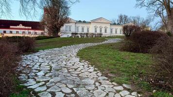 A scenic stone pathway weaves through lush greenery, guiding visitors towards a charming and historic estate photo
