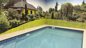 A peaceful and serene poolside view that showcases a vibrant garden as well as a charming house nearby photo