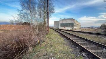 A longabandoned structure sits lonely next to disused railway tracks, thoroughly surrounded by wild nature photo