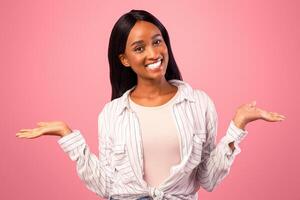 Young black woman comparing options, making scales with her hands, holding invisible objects on pink studio background, mockup. African American lady advertising your products photo