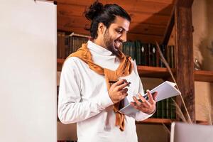 Online Teaching Concept. Indian Teacher Guy Having Web Class Explaining English Language Rules To Webcam Standing Near Blackboard At Home. Distance Study, Education And E-Teaching. Selective Focus photo