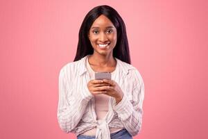 Portrait of smiling young black woman browsing web on smartphone. Pretty African American lady using mobile phone for online studies or work, chatting with friends on internet photo