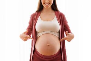 Happy Pregnancy. Positive Young Woman Pointing At Her Naked Pregnant Belly With Two Hands, Standing Against Window At Home, Cheerful Expectant Mother Enjoying Prenatal Time, Copy Space photo