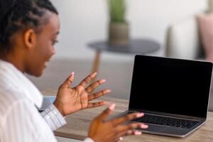 Back view of african american lady employee having online conference with her business team from home, looking at computer with blank screen, talking and gesturing, mockup, copy space photo