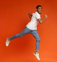 Emotional motivated african-american man running to aim on air, jumping on orange background photo