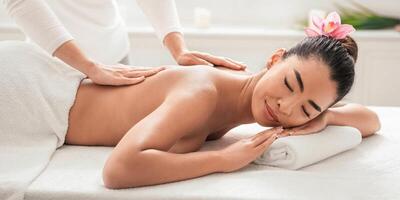 Relaxed asian woman enjoying body massage at spa, getting treatment with professional masseur in beauty parlor, lying on table with closed eyes, having wellness day, side view with free space photo
