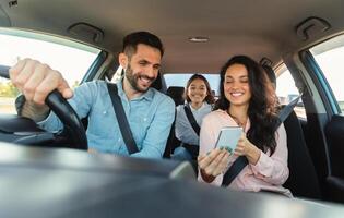 Car navigation app. Happy woman showing gps application on cellphone to driver man, family travelling and navigating vehicle with gadget, enjoying weekend trip photo
