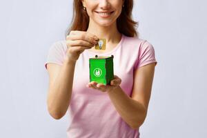 Light Bulb Disposal. Woman Putting Card With Lightbulb Icon Into Wooden Toy Trash Container, Agitating For Zero Waste Living And Garbage Sorting, Standing Over Gray Studio Background, Cropped Image photo