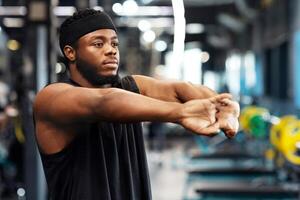 Athletic black guy stretching hands and fingers in gym and looking at copy space. Muscular african american bearded sportsman warming up before workout. Active lifestyle concept photo