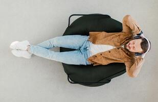 Top View Of Relaxed Guy Wearing Wireless Earphones Listening To Music Or Online Podcast Resting With Eyes Closed Lying In Chair At Home. Weekend Leisure And Relaxation Concept photo