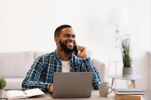 Smiling Black Businessman Talking On Phone Sitting At Workplace In Modern Office. Mobile Business Communication And Entrepreneurship. Man Having Cellphone Conversation At Work. photo