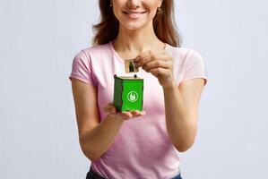 Conceptual Image For Waste Sorting. Woman Putting Card With Drinking Glass Icon Into Small Wooden Toy Garbage Container, Unrecognizable Lady Standing Over Light Background In Studio, Free Space photo