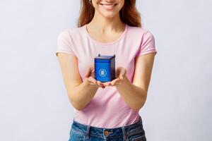 Smiling Young Woman Holding Small Blue Toy Recycle Bin For Paper Waste, Standing Over Light Studio Background, Conceptual Image For Garbage Sorting And Trash Recycling, Cropped Shot With Free Space photo