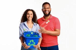 Diverse Family Couple Holding Box With Recycle Symbol Putting Used Plastic Bottle To Garbage Container Posing Standing Over White Background, Smiling To Camera. Waste Sorting, Junk Disposal photo