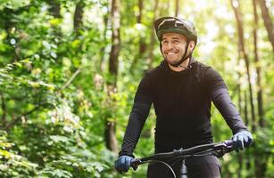 Joyful male bicyclist cycling in mountain forest in sun flares, enjoying the view, copy space photo