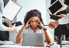 Multitasking. Overworked Afro Businesswoman Sitting Touching Head Ignoring Colleagues Tired Of Multiple Tasks At Work In Modern Office. photo
