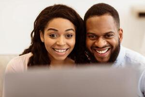 Technology Concept. Closeup portrait of smiling excited black couple using laptop computer, having online conference with friends or family, watching or movie spending time at home photo