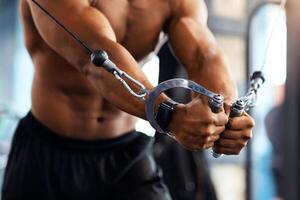 Cropped of black man athlete training triceps on block exerciser in gym, copy space. Unrecognizable african american bodybuilder having workout at modern gym, using crossover machine photo
