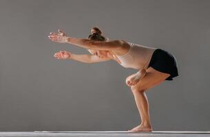 Woman performing advanced yoga pose in studio, balancing on one leg with arms extended, demonstrating flexibility, balance, and focus in a minimalist fitness environment. photo