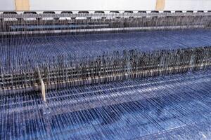 Automated loom weaving blue textile, detailed view of industrial warp threads and heddles. photo