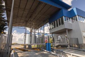 Modern Industrial Checkpoint Entrance with Security Gate and Silos at Logistics Facility on Sunny Day photo