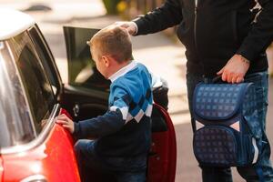 Boy enters car for school as parent holds backpack, family morning routine, back to school concept photo