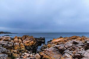 a view of a rocky shoreline with a lighthouse in the distance photo