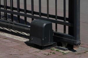 Automated sliding iron gate and motor on a brick driveway photo