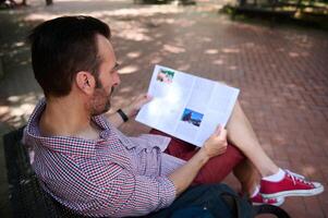 Man Relaxing on Bench while Reading a Magazine in Outdoor Park Setting photo