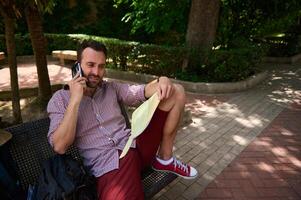 Man Sitting on a Bench in a Park Using a Phone and Reading a Map photo