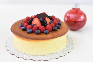 Fluffy Japanese Cheesecake topped with strawberries, raspberries, blueberries, and blackberries with bottle of red berry sauce closeup side view of delightful and popular dessert photo