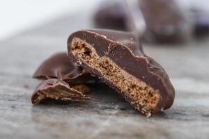 Decadent Chocolate Covered Biscuit Piece, broken in half to clearly show its textured, crumbly interior with hick layer of chocolate coating isolated on marble closeup side view of sweet treat photo