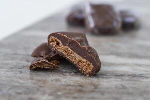 Decadent Chocolate Covered Biscuit Piece, broken in half to clearly show its textured, crumbly interior with hick layer of chocolate coating isolated on marble side view of sweet treat photo