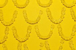 Clear dental aligners on colored yellow background, close-up side view from above. Pattern of clear braces photo