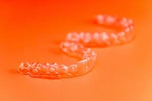 Invisible teeth retainers lie on a bright orange background. Close-up of a modern way to straighten teeth photo