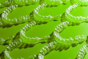 Invisible transparent aligners for teeth alignment of the lower and upper jaw. Wax models of teeth, top view, on a green background photo