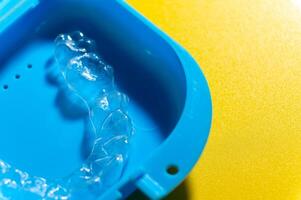 Close-up Blue plastic case with transparent brackets on a peach background. Invisible removable retainers for orthodontic treatment photo