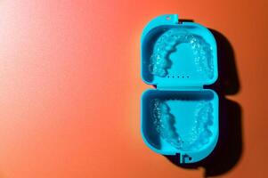 Blue plastic case with transparent brackets on a peach background. Invisible removable retainers for orthodontic treatment photo